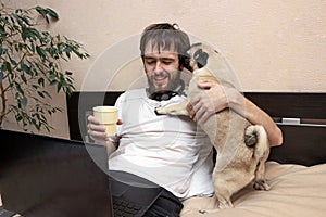 Man lying on bed looking at laptop, his pug dog interfere, licking his face