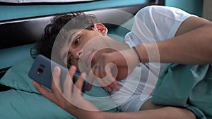 Man lying in bed, looking scared and shocked at smartphone screen, reading message with concerned face.