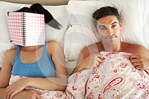 Man Lying In Bed Next To Woman Reading Book