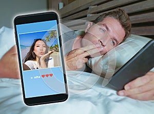 Man lying on bed sending good night kiss text with mobile phone having internet video call with Asian Chinese girlfriend in long