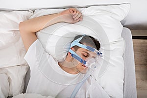 Man Lying On Bed With Sleeping Apnea And CPAP Machine