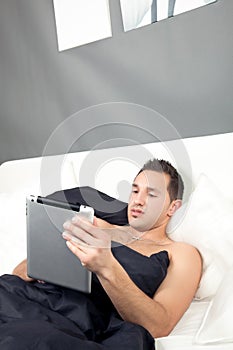 Man lying in bed working on his tablet photo