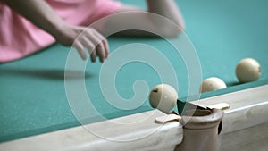 A man lying on a billiard table plays with billiard balls, rolls them into a pocket, close-up