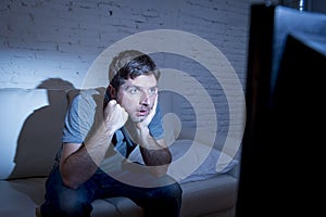 Man lying on couch at living room watching tv holding remote control looking mesmerized