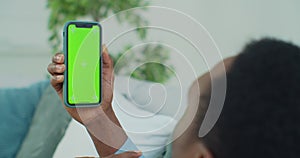 Man lying on couch with modern smartphone in his hand while looking on mock up screen with trecking markers on it