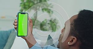 Man lying on couch with modern smartphone in his hand while looking on mock up screen with trecking markers on it