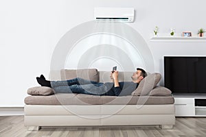 Man Lying On Couch Under Air Conditioner Using Tablet