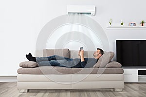 Man Lying On Couch Under Air Conditioner Using Tablet photo