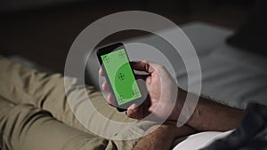 Man lying on couch using smartphone with chroma key green screen, scrolling