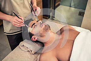 Man lying down during traditional facial treatment at beauty center