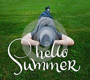 Man lying in a field on green grass with the hat over his face and text Hello summer. Calligraphy lettering hand draw