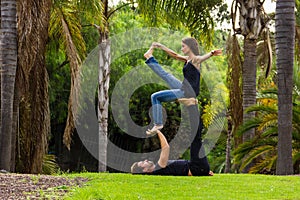 Man lying on grass as base for woman as flyer in acro yoga class in park