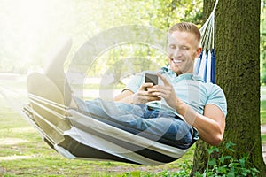 Man Lying In Hammock Using Mobile Phone