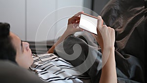 Man lying on hissed under blanket and using smartphone at night.
