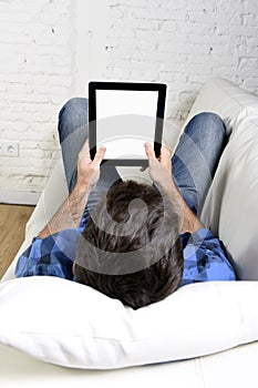 Man lying on home couch using digital tablet pad in portable internet technology