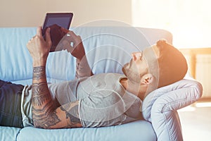 Man lying on sofa with digital tablet at home