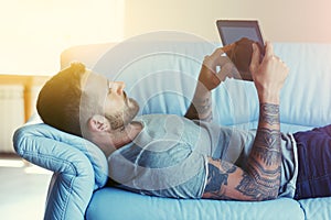 Man lying on sofa with digital tablet at home