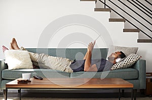 Man Lying On Sofa At Home Wearing Headphones And Watching Movie On Digital Tablet