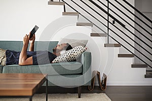 Man Lying On Sofa At Home Wearing Headphones And Watching Movie On Digital Tablet