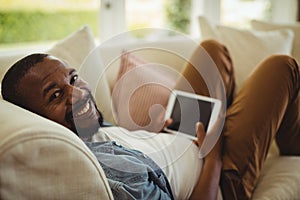 Man lying on sofa and using digital tablet
