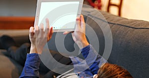 Man lying on sofa and using digital tablet in living room