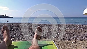 A man lying on a sunbed facing the seashore on the pebble beach.