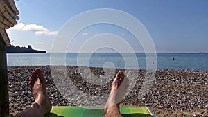 A man lying on a sunbed facing the seashore on the pebble beach.