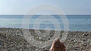 A man lying on a sunbed facing the seashore on the pebble beach.