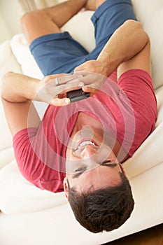 Man Lying Upside Down On Sofa Sending Text Message