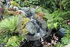 A man made artificial stream ending in a pond decorated with an assortment of surrounding flora flowers