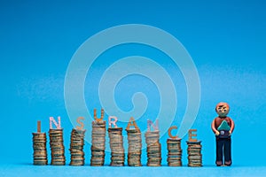 Man made from plasticine holding a house model to the right of a bunch of columns made from coins, with the word insurance placed