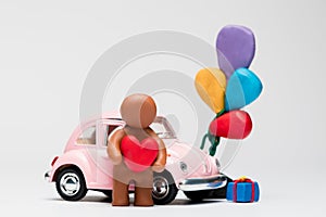 Man made from plasticine next to a car with balloons on white background, aligned in the center