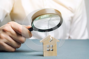 A man with a magnifying glass looks at a house with a crack. Damage assessment home and insurance risks