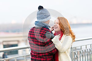 Man makes funny ginger woman in red scurf. Guy cares about woman. Woman happy to meet man in city. photo