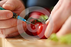 Man makes an injection into a red tomato, hands close-up