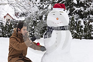 A man makes a snowman in his yard. T