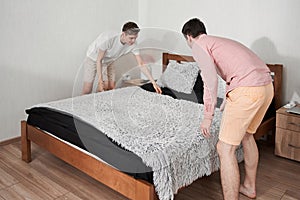 Man making bed and organizing room in morning with his boyfriend