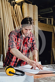 Man making draft plan using pencil on the table with workshop on background.