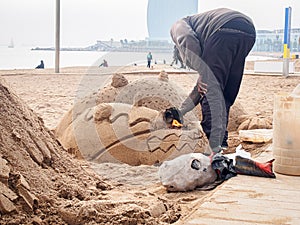 Man is making a dragon sand sculpture on the Sant Miguel beach in Barcelona