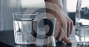 man making drink in tumbler glass on black oak table