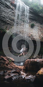 Man making an extreme leap from a rock with  Fall Creek Falls in the background