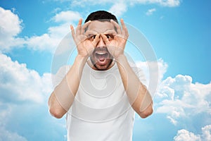 Man making finger glasses over blue sky