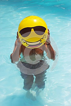 Man is making fun in the pool, having inflatable yellow ball infront of his face