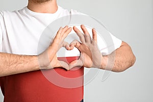 Man making heart with his hands on light background