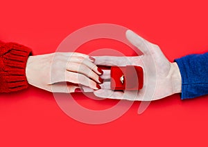 Man making marriage proposal. Male hand giving a gift box with engagement ring on red background. Close-up. Top view