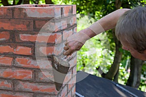 A man making masonry works, working with a trowel and making a chimney of red bricks