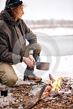 man making meal on campfire in forest,in winter forest, nature. caucasian guy travelling