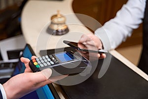 Man making payment with phone, receptionist holding credit card reader in hotel