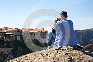 Man making photo near The Holy Monastery of Varlaam on the cliff at Meteora rocks, Greece