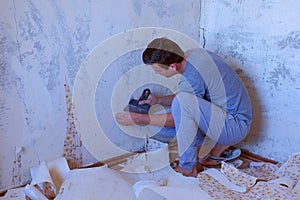 Man is making renovation removing wallpapers from wall, construction work.